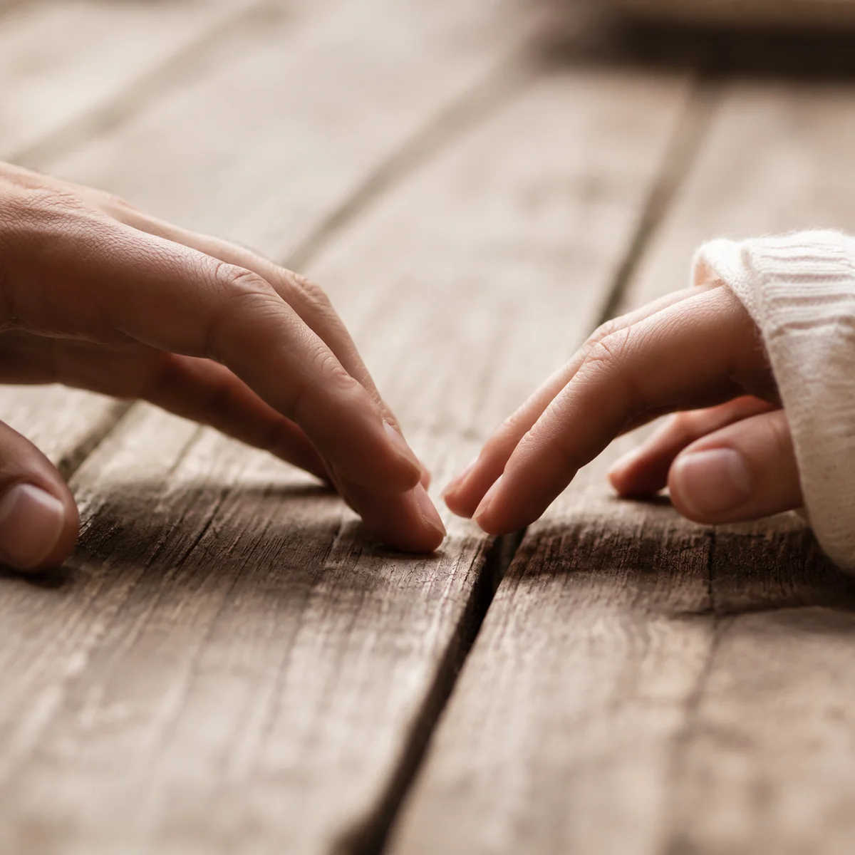 Close-up of two hands almost touching on a weathered wooden table, capturing vulnerability and anticipation in soft natural light