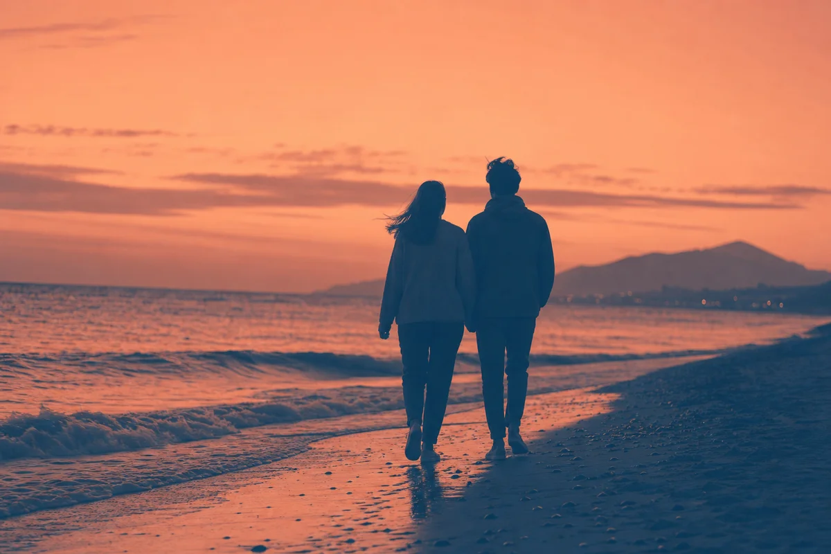 Two figures walking side by side along a shoreline in warm coral and steel blue duotone